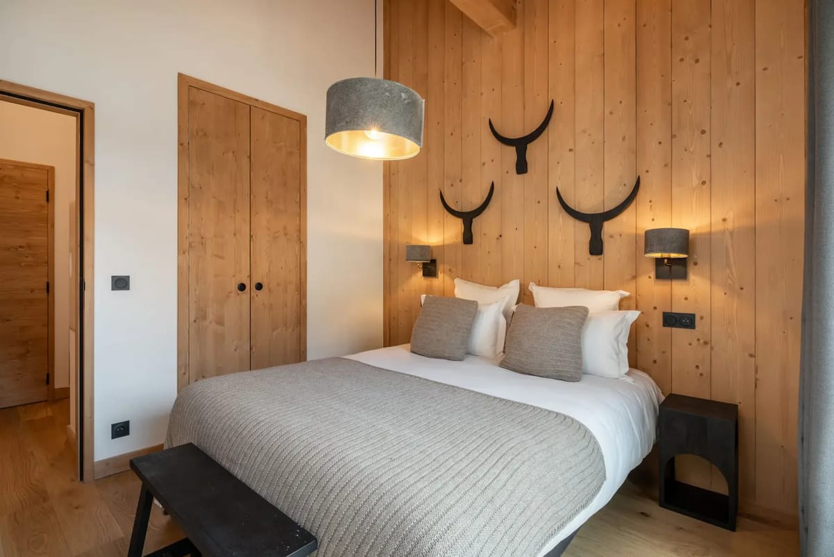 Cozy bedroom with wooden walls, a double bed, decorative antlers, and a balcony view of mountains.