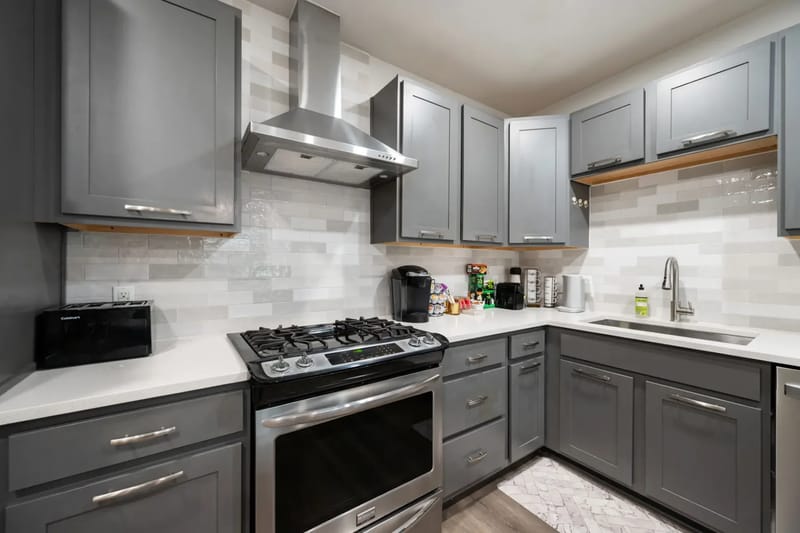 Modern kitchen with gray cabinets, stainless steel appliances, gas stove, backsplash, coffee maker, and utensils.