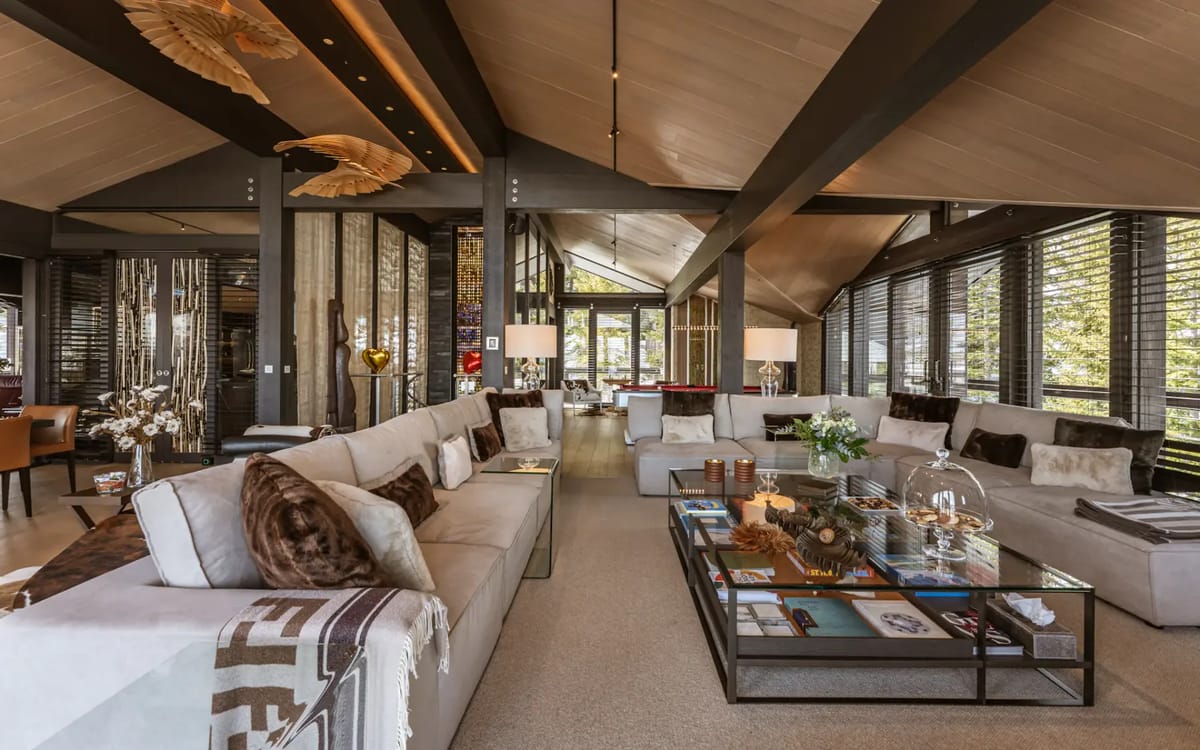 Spacious modern living room with beige sofas, a glass coffee table, wooden ceiling and large windows.
