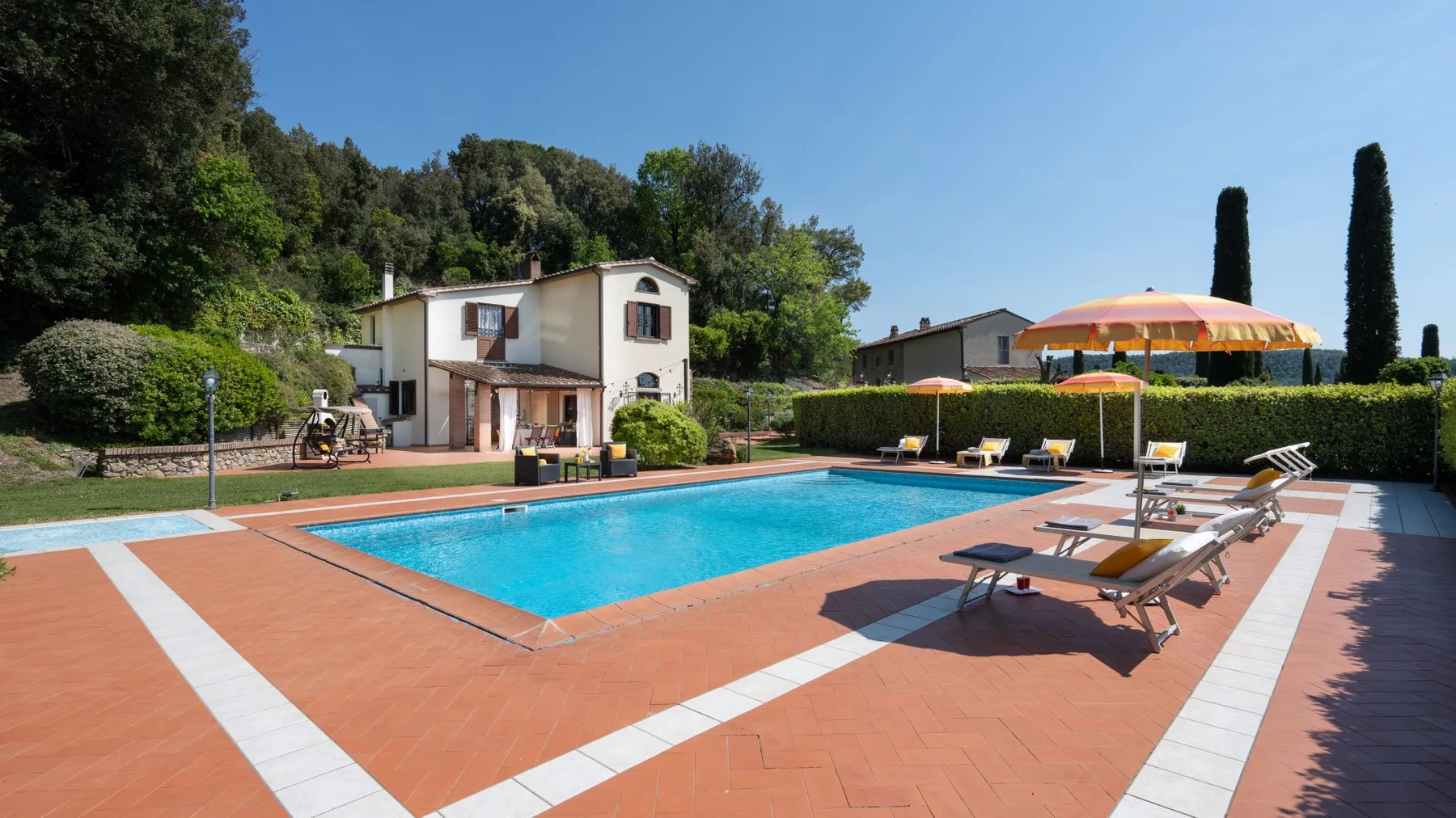 Una piscina al aire libre está junto a una casa, con tumbonas en el patio.