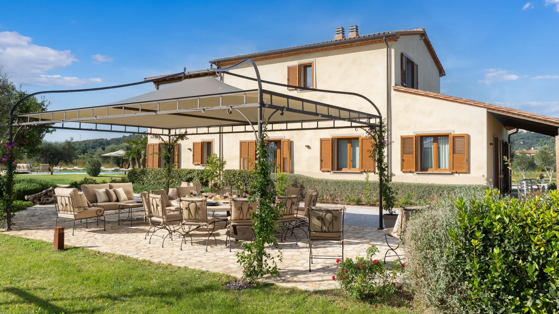 A house with a shaded patio and outdoor seating overlooks a garden.