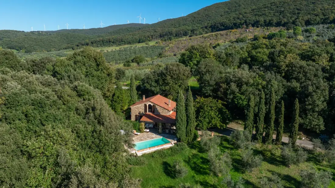 Una casa con piscina se encuentra entre colinas boscosas.