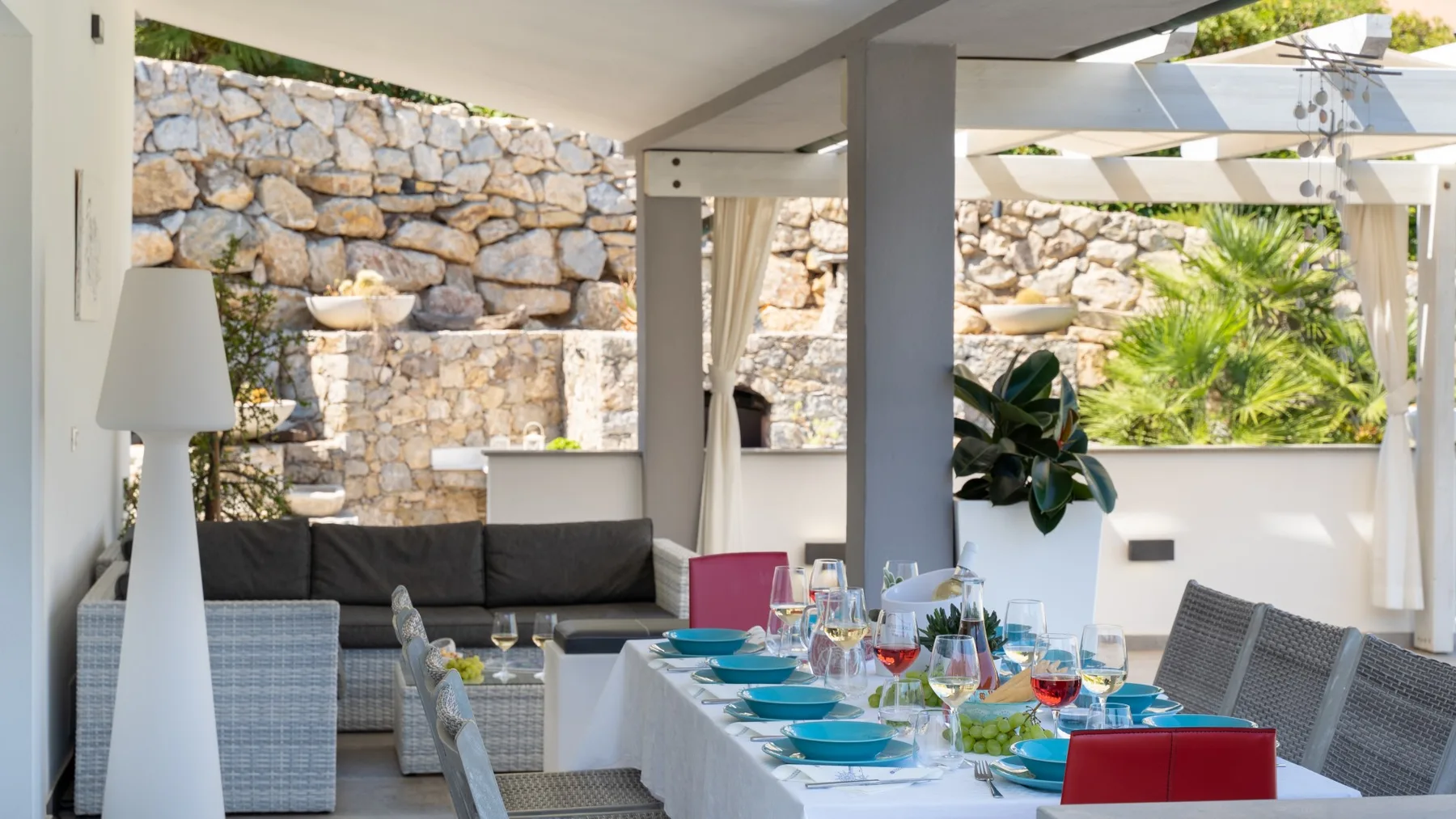 Comedor exterior cubierto con una mesa puesta y asientos junto a un muro de piedra.