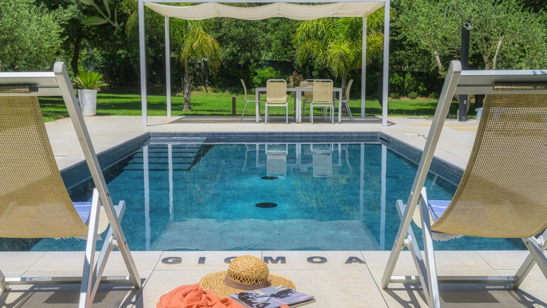 A swimming pool sits beneath a white canopy, with loungers in the foreground.