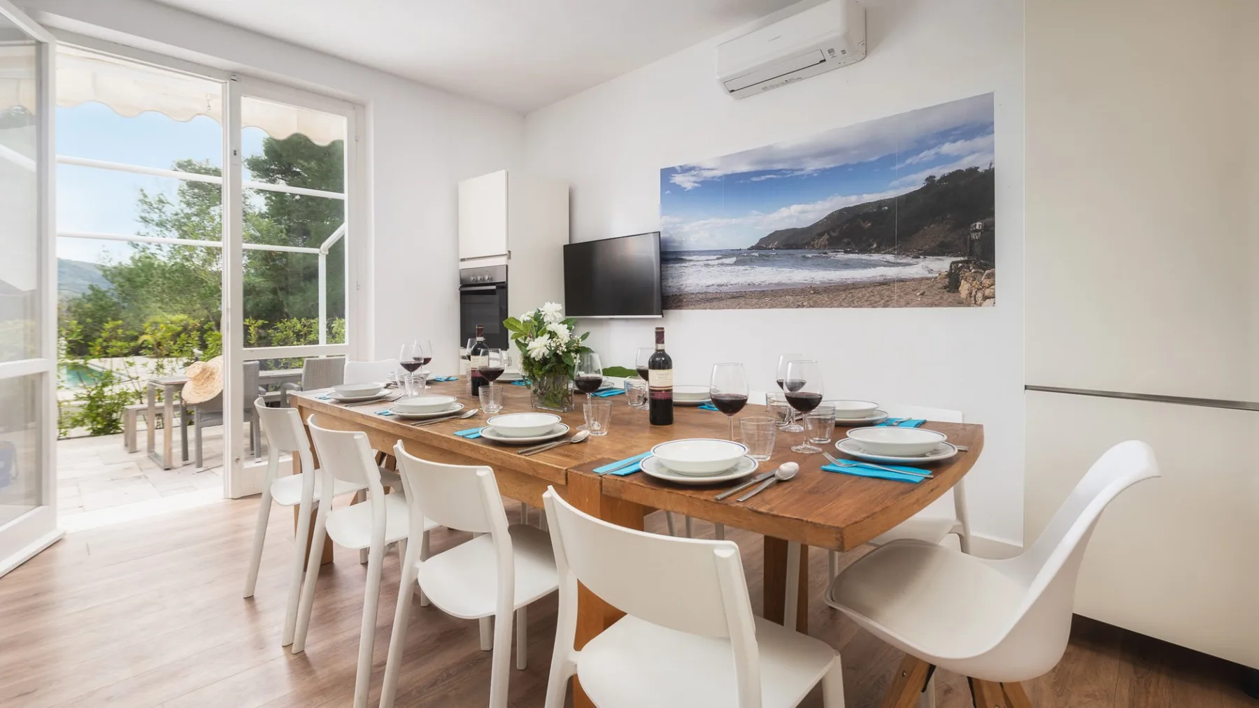 Un comedor luminoso con una mesa de madera puesta junto a grandes ventanas.