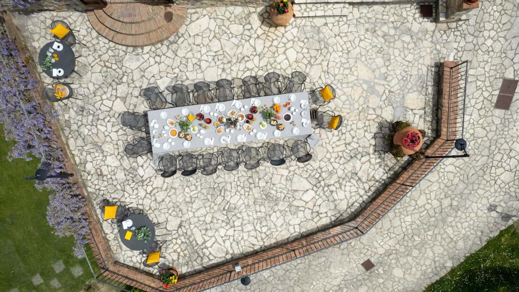 Comedor al aire libre con una mesa larga sobre un patio pavimentado de piedra.
