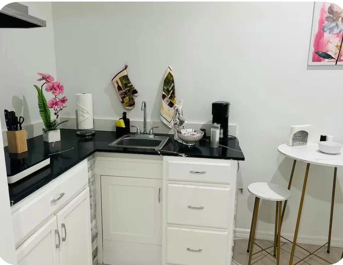 A compact kitchen with a black countertop, sink, and white cabinets.