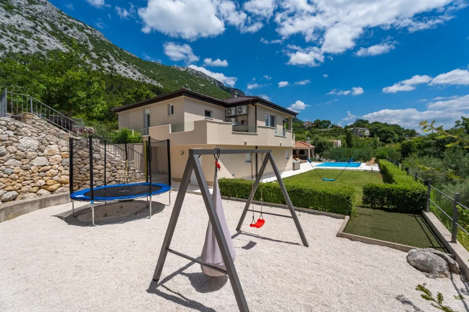 Fenced playground with trampoline, swing, badminton area and mini golf