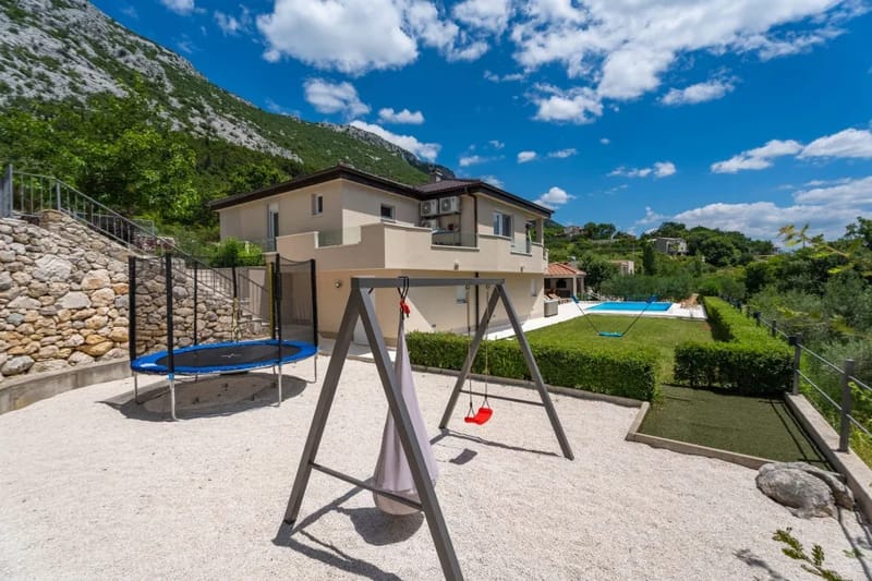 Fenced playground with trampoline, swing, badminton area and mini golf