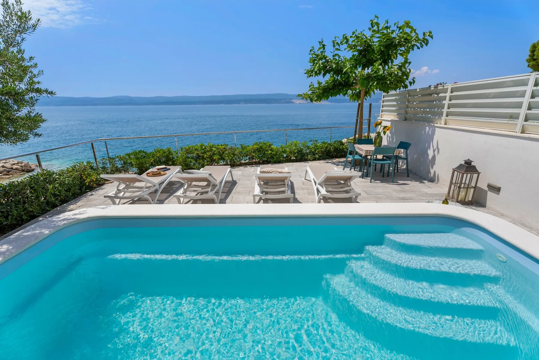 Outdoor poolside patio with lounge seating beside a waterfront view.