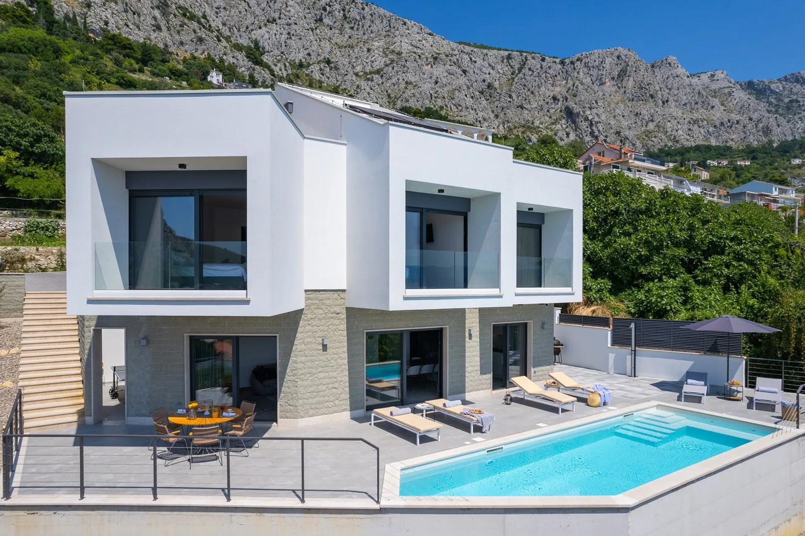 Modern villa exterior with a swimming pool and mountain backdrop.