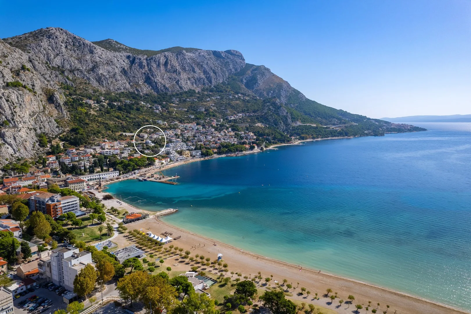 Aerial view of a coastal town beside a curved beach and mountains.