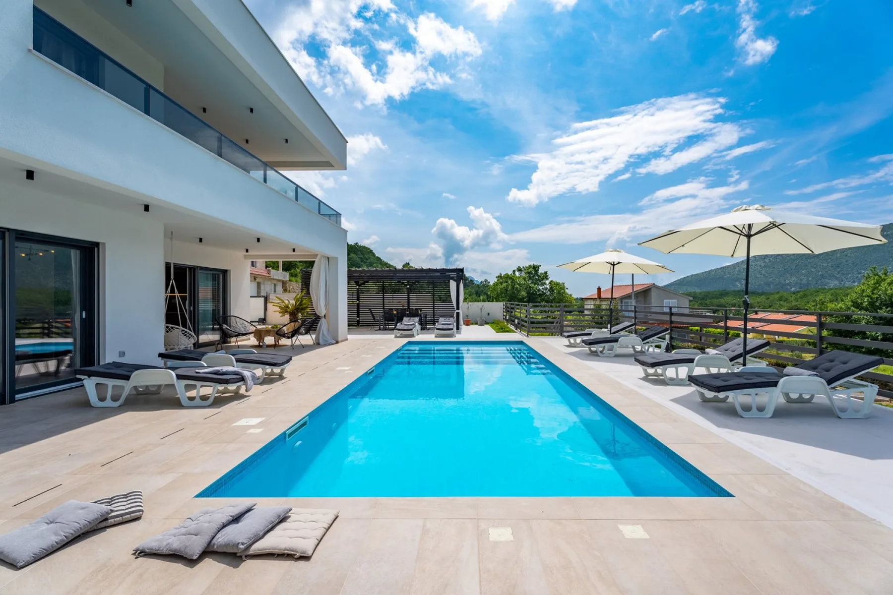 An outdoor swimming pool beside a modern building, with loungers and umbrellas.