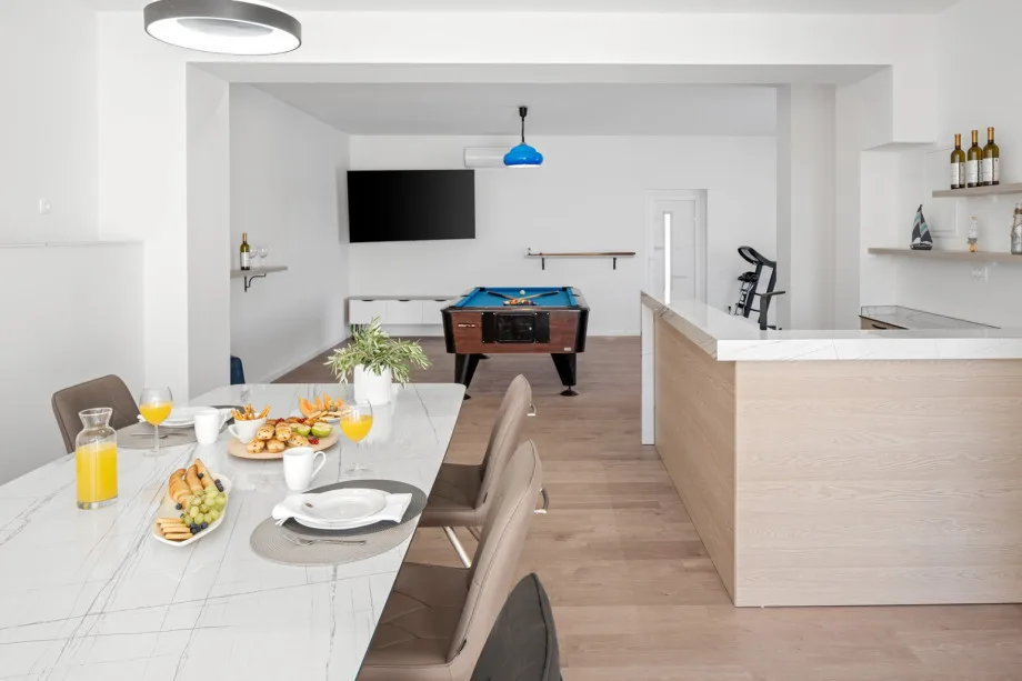 Zona de ocio cubierta con mesa de comedor, cocina de verano, mesa de billar, cinta de correr y bicicleta estática