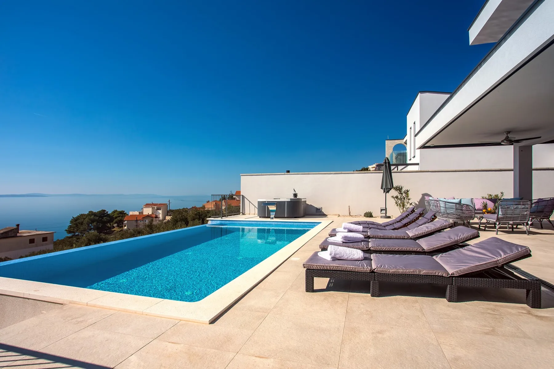 A rooftop pool terrace with reclining loungers and a view of the sea.