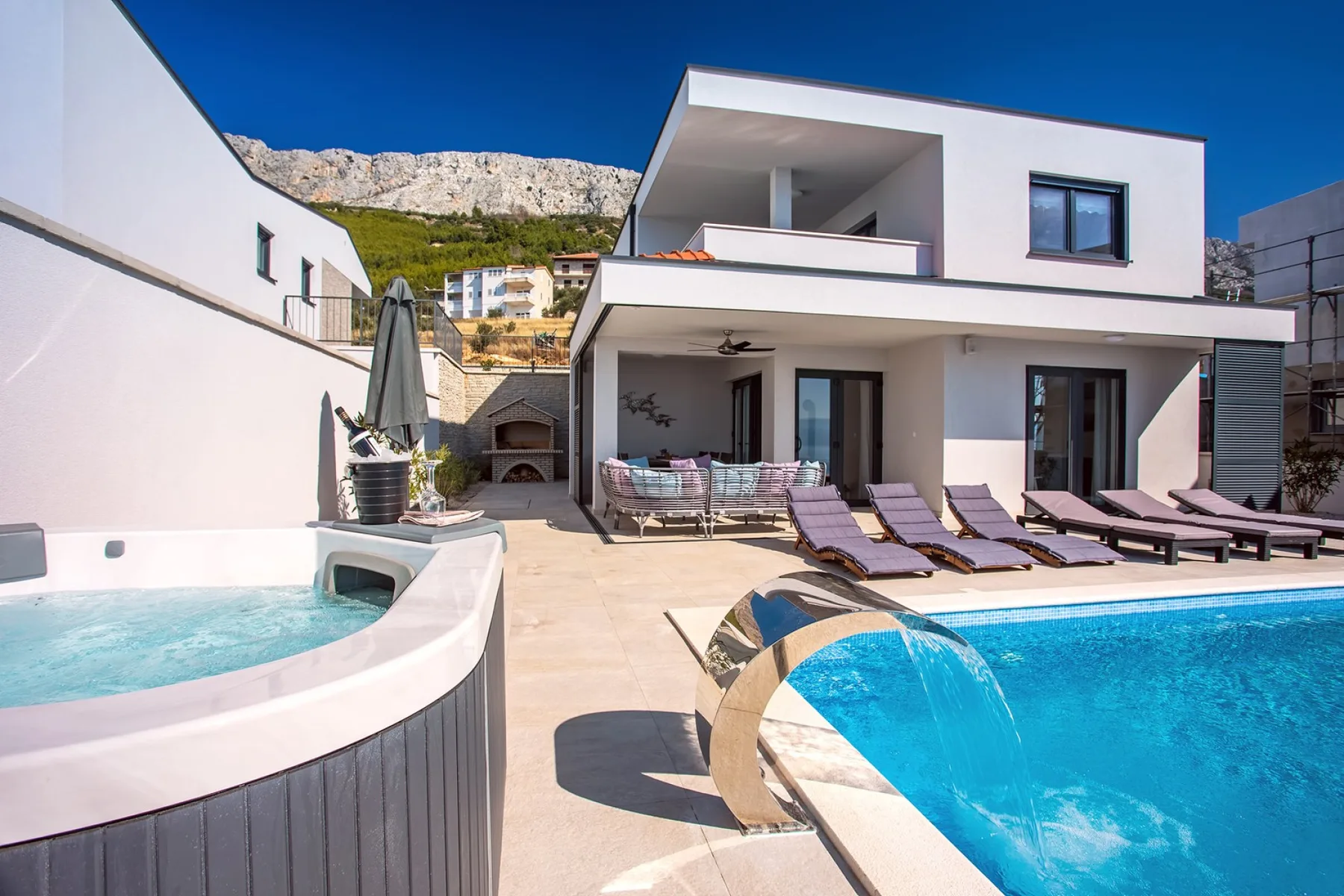 A swimming pool and raised spa sit beside a modern white house.