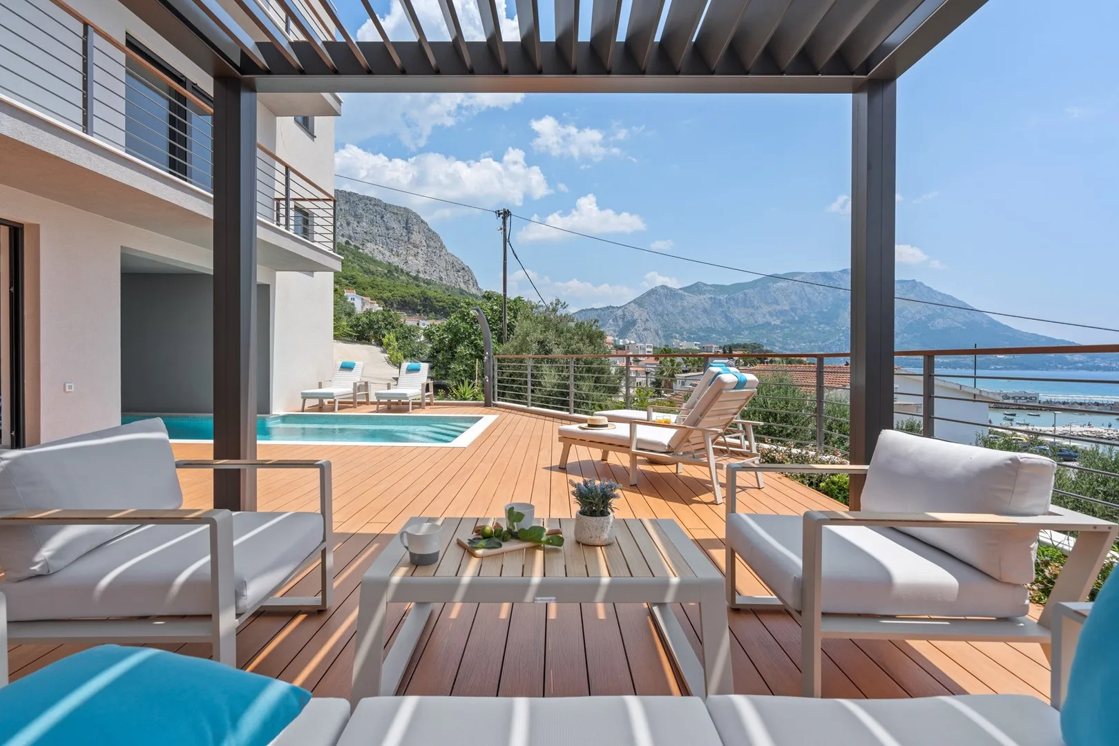 A furnished outdoor terrace overlooks a swimming pool and mountain scenery.