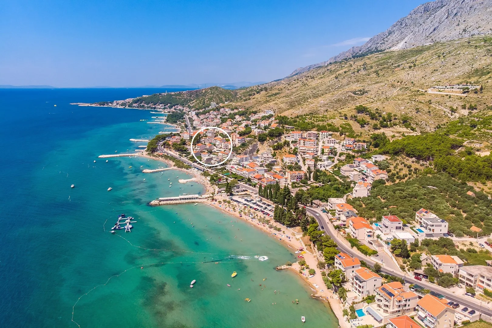 A coastal town stretches along a turquoise shoreline beneath a dry mountain slope.