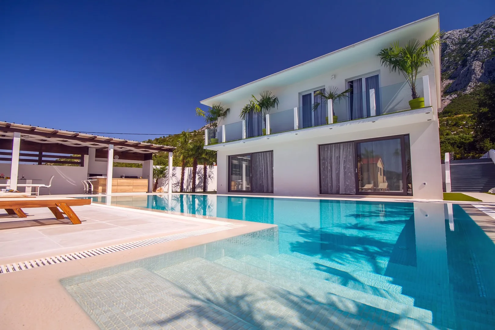 A modern house stands beside a swimming pool and a shaded patio.