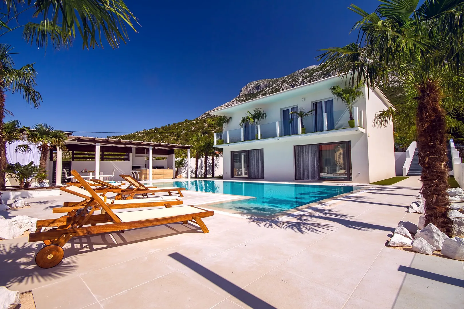 Una villa moderna junto a una piscina, con tumbonas en el patio.