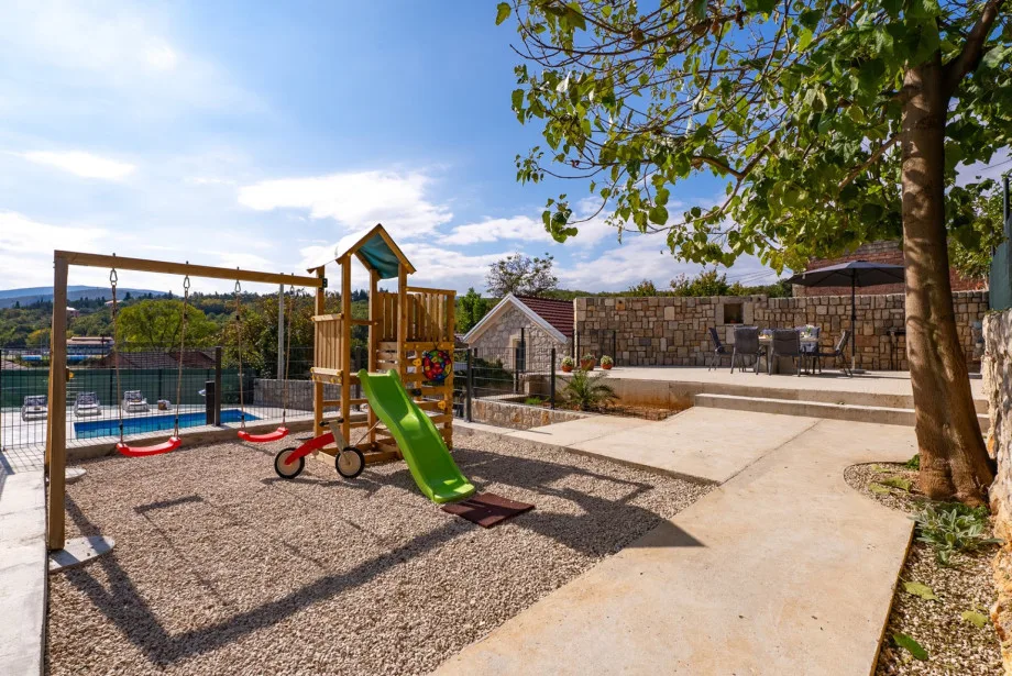 La estructura infantil para trepar con un tobogán y un columpio bajo un árbol.