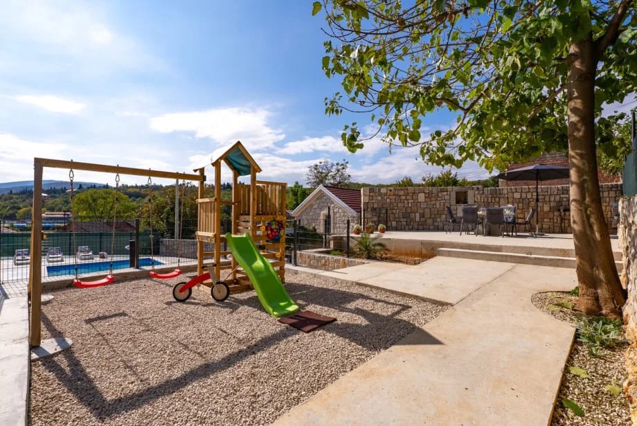 La estructura infantil para trepar con un tobogán y un columpio bajo un árbol.