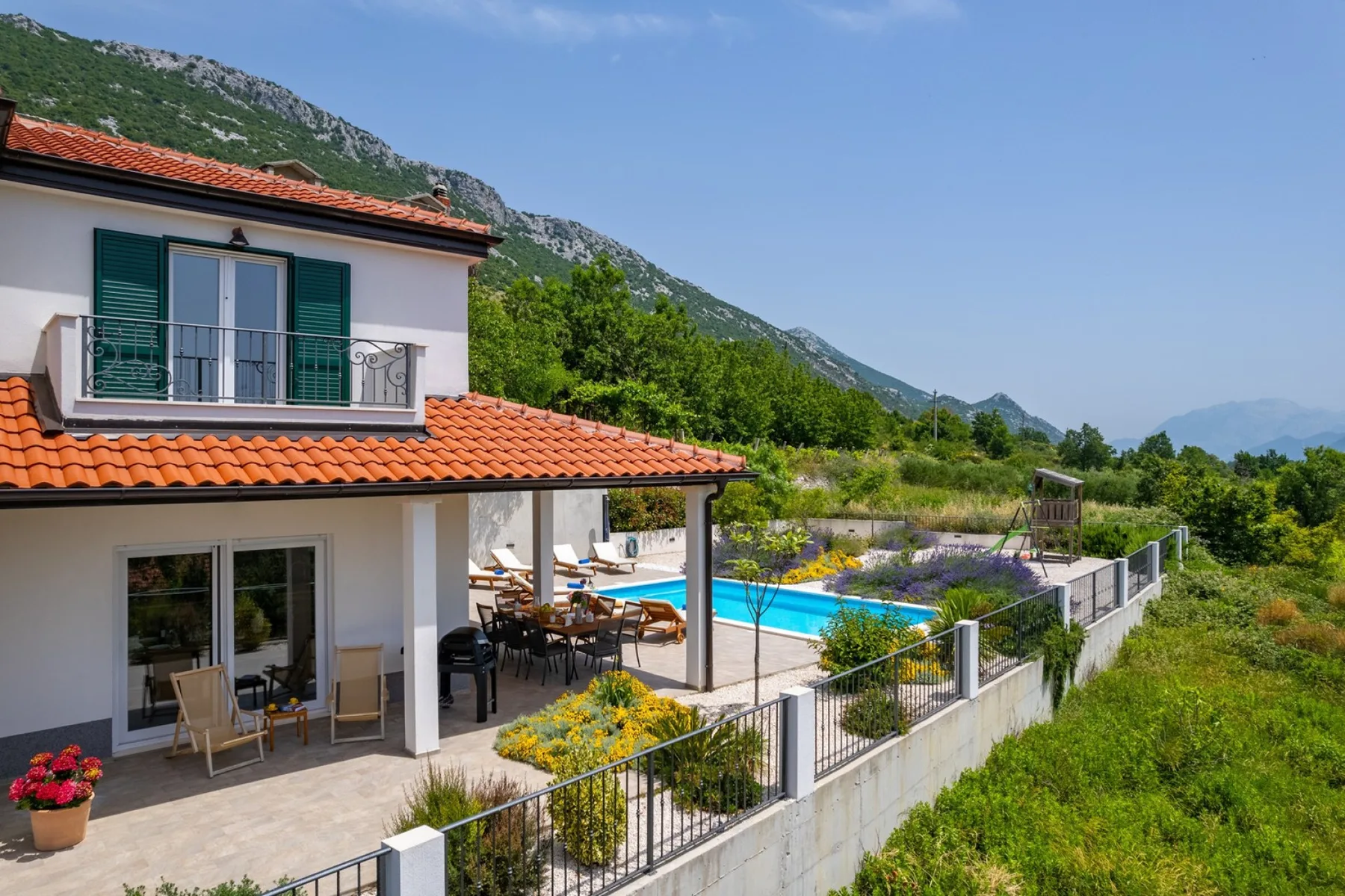 Una villa blanca con patio cubierto da a una piscina y colinas verdes.