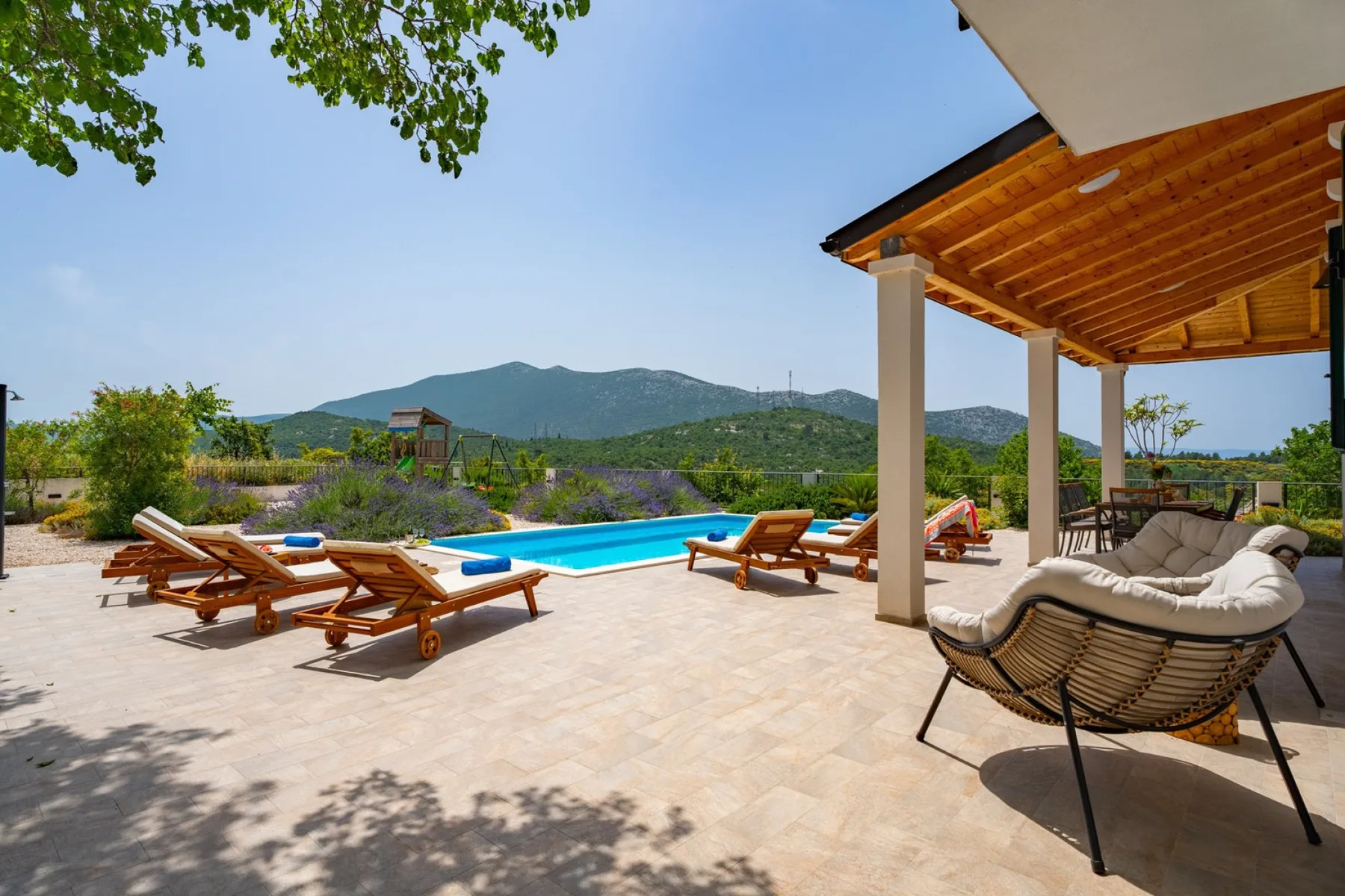 Una piscina al aire libre y tumbonas están junto a un patio sombreado.
