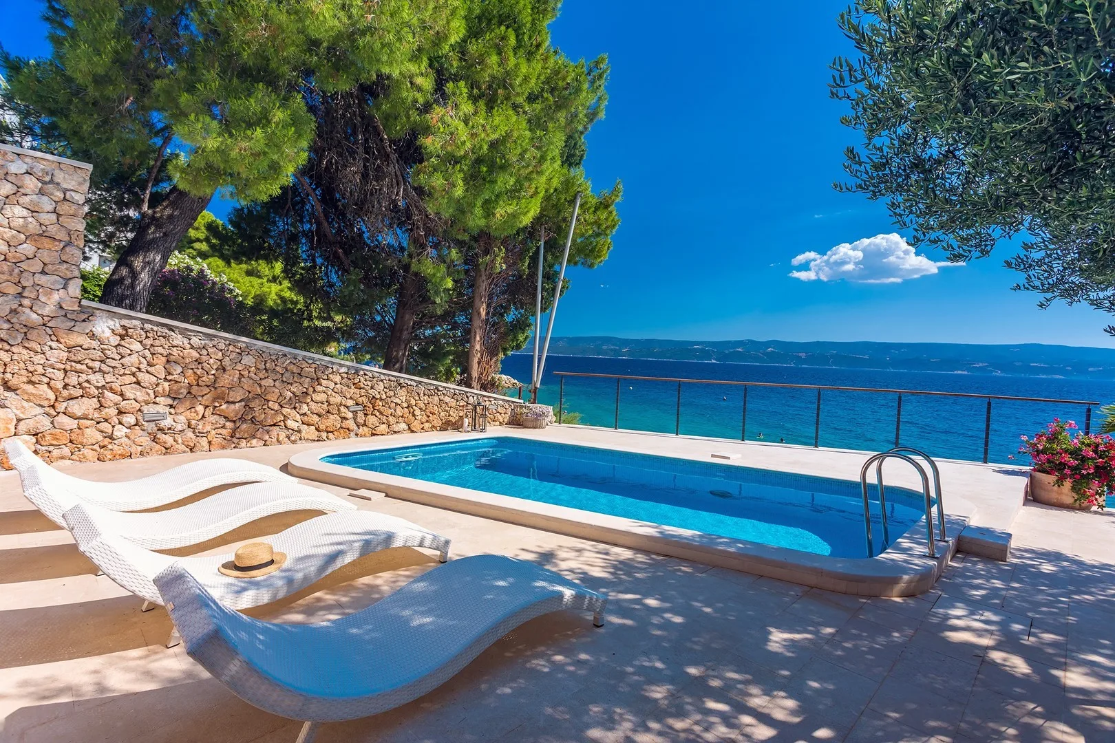 An outdoor pool terrace overlooks the sea, with reclining loungers beside the water.
