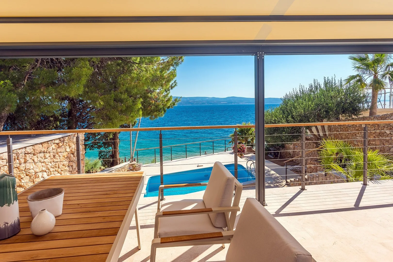 A sunny terrace overlooks a swimming pool and the sea.