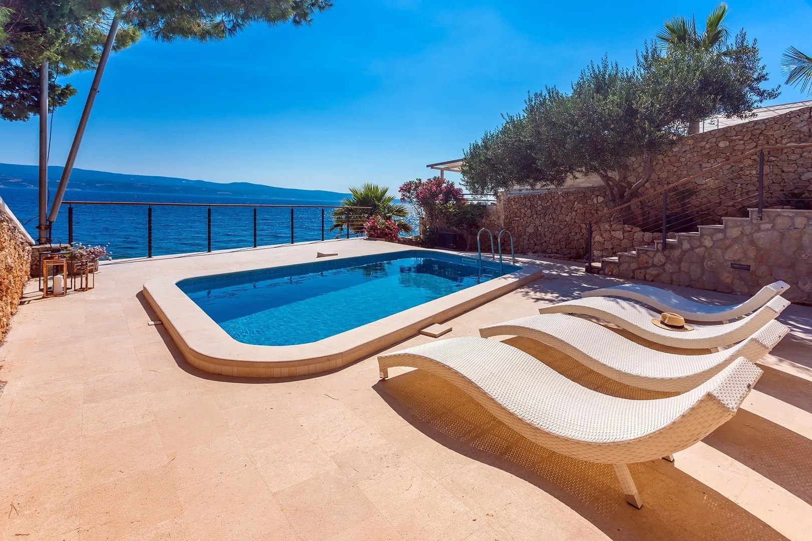 A poolside terrace overlooks the sea, with lounge seating beside the water.