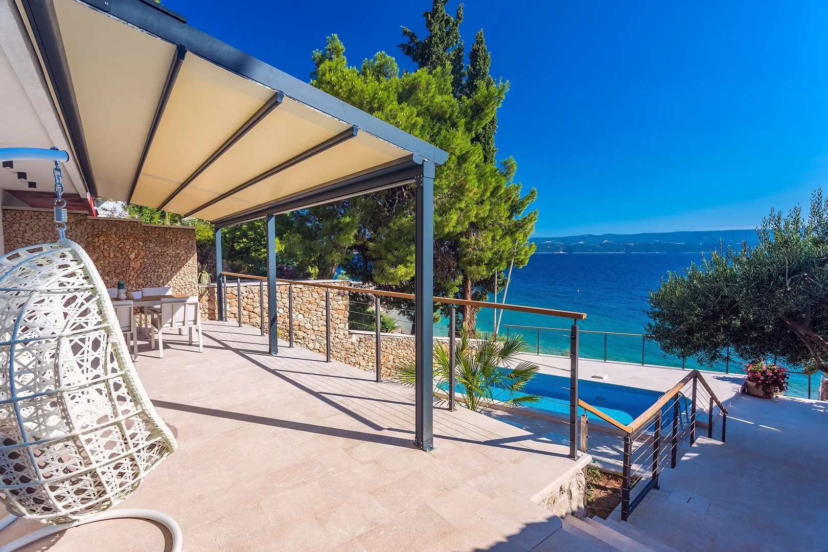 A shaded terrace overlooks a pool and the sea.