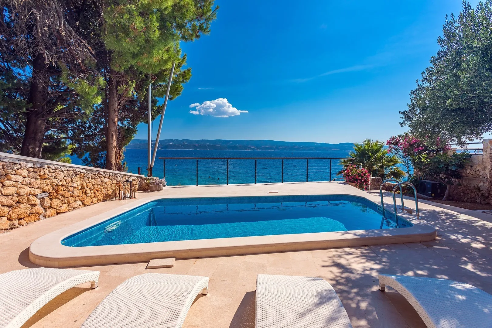A swimming pool overlooks the sea, with lounge seating on the surrounding patio.