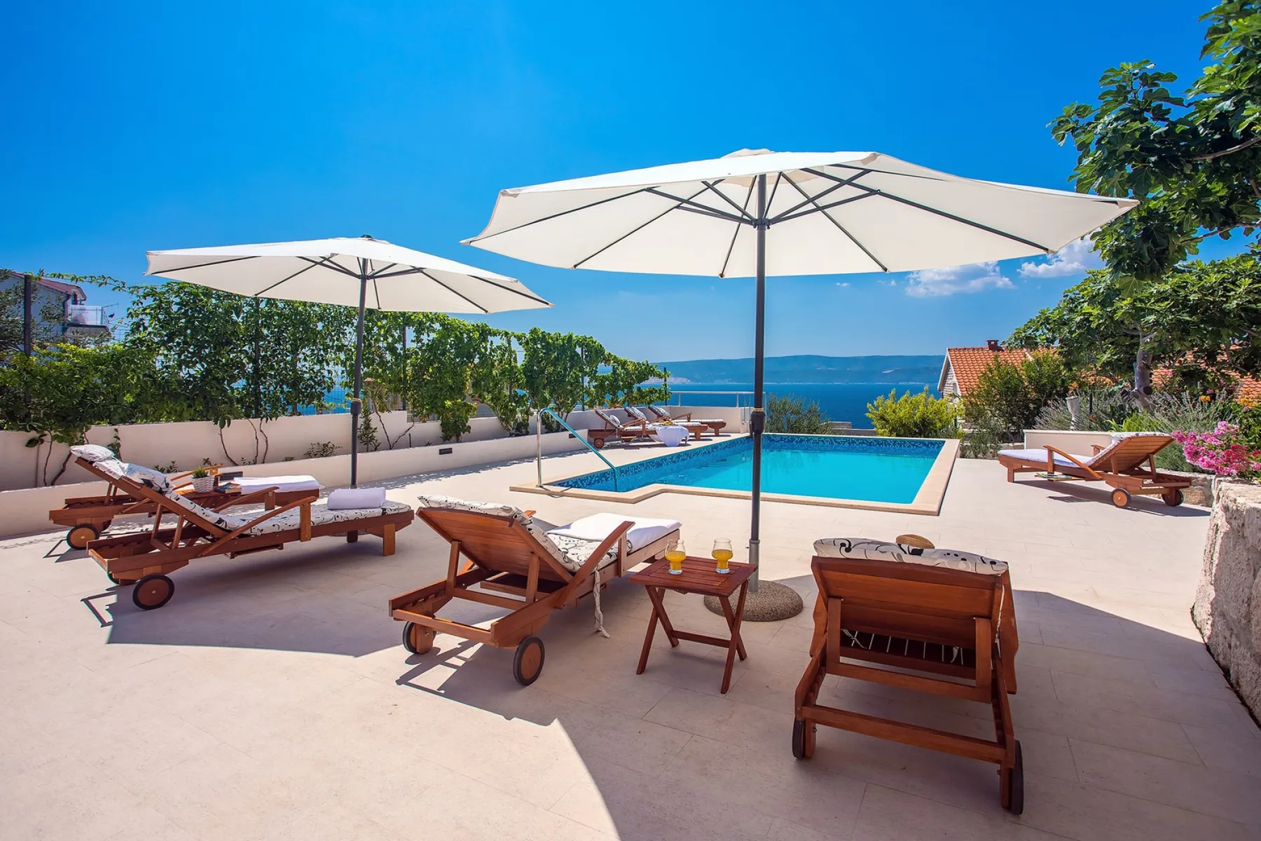 An outdoor pool area with sun loungers and a view of the sea.