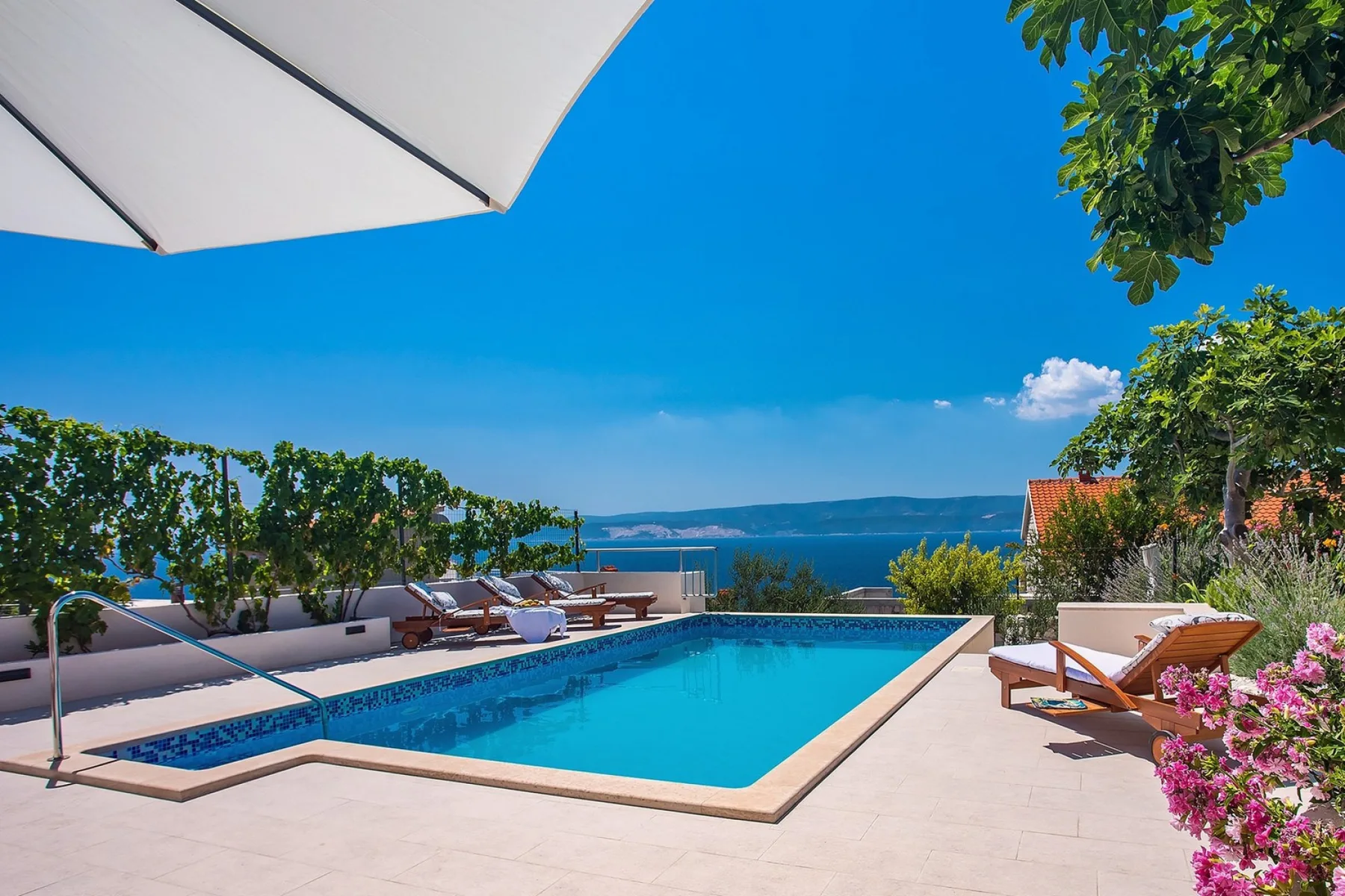 An outdoor swimming pool with lounge seating and a view of the sea.