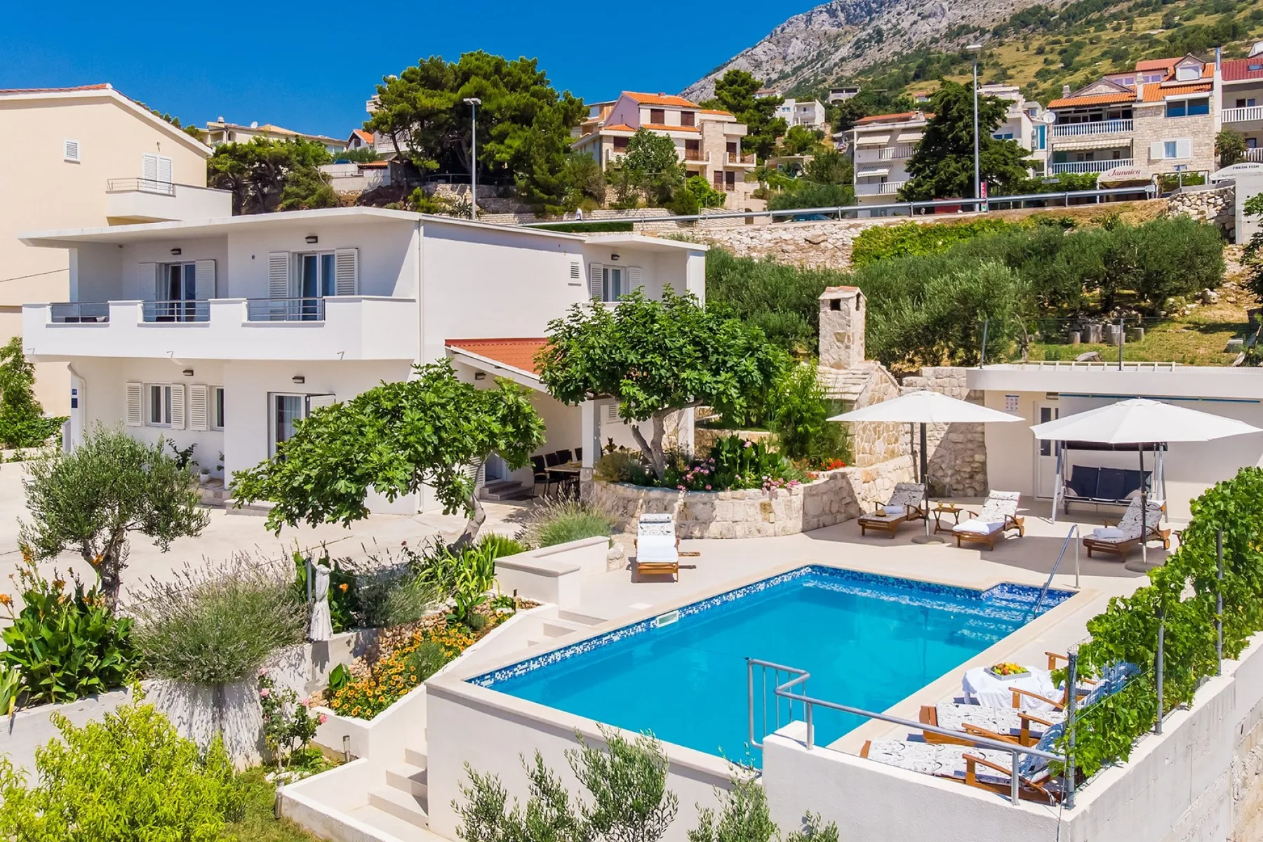 A modern villa beside a swimming pool, with loungers and umbrellas on the terrace.