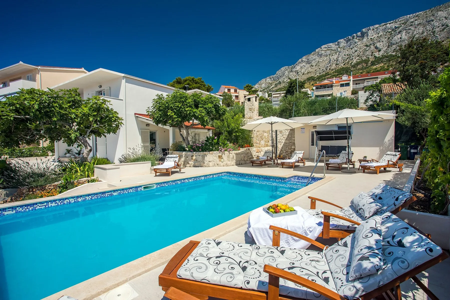 An outdoor swimming pool is surrounded by lounge seating and patio umbrellas.