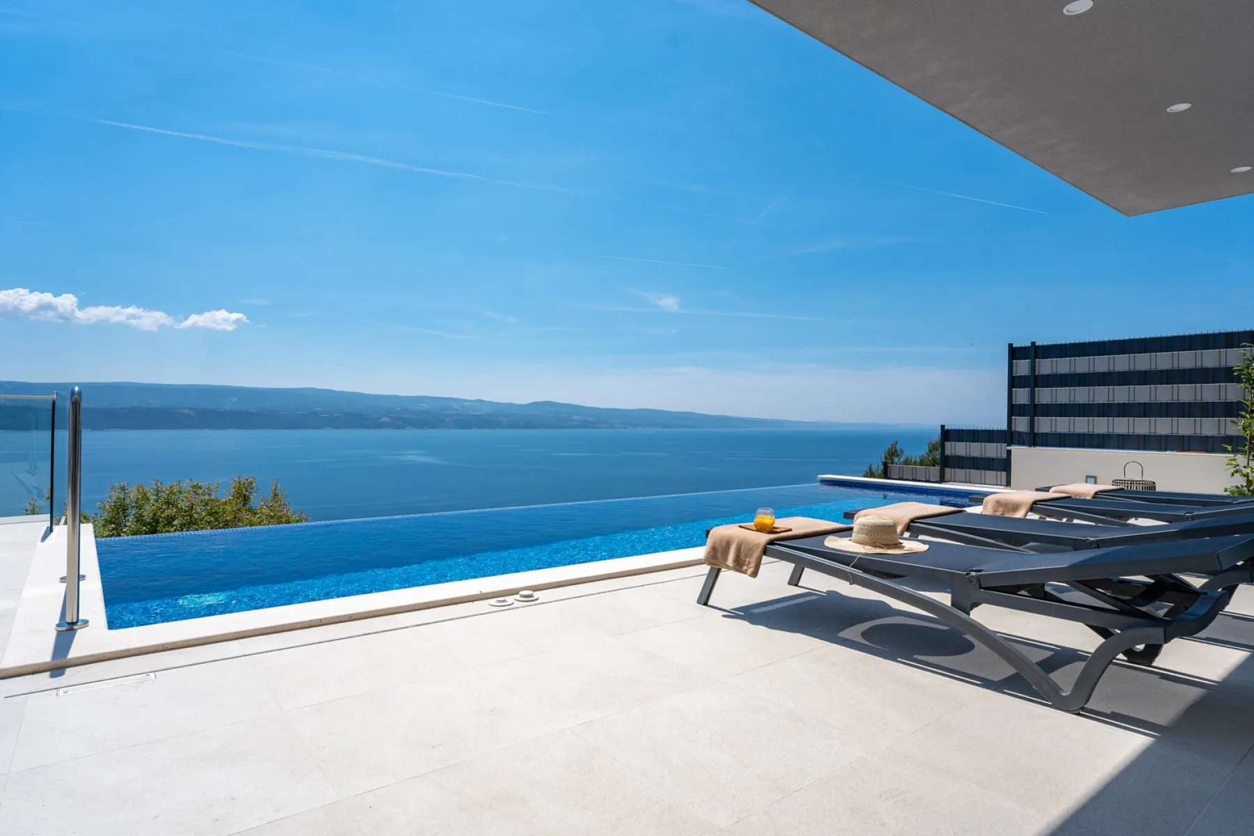 Terraza exterior junto a la piscina con tumbonas frente al mar.