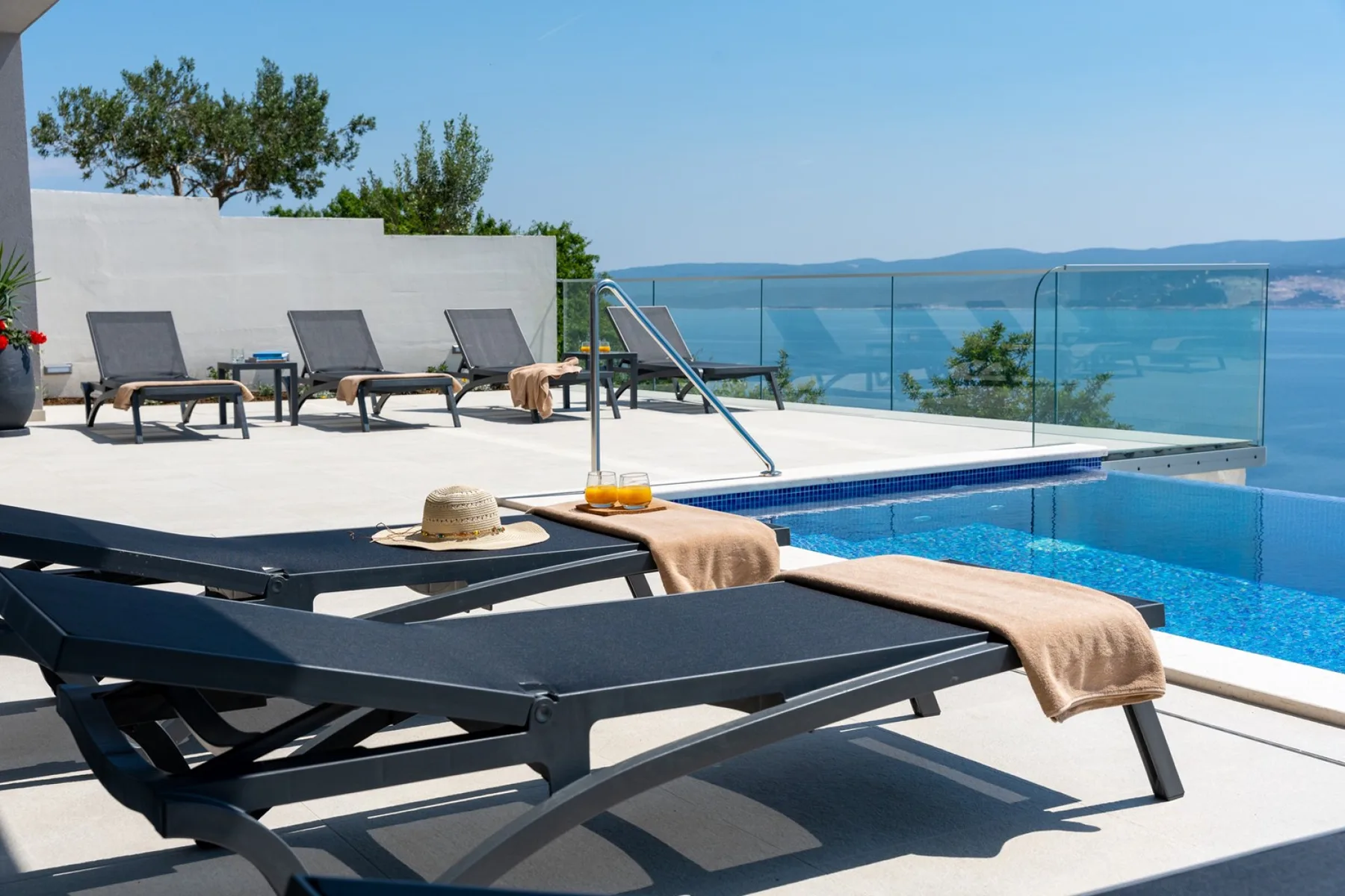 A poolside terrace with lounge seating overlooks the sea.