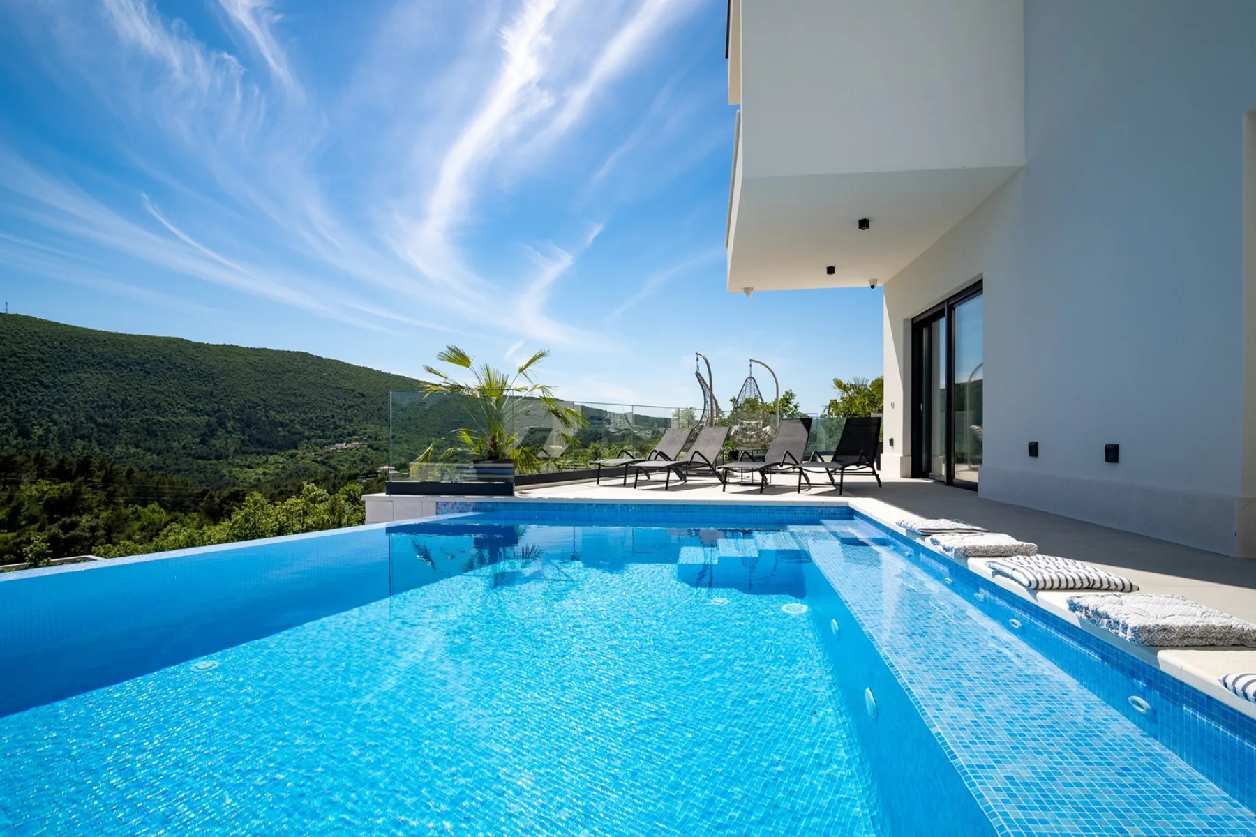 An outdoor swimming pool beside a modern building, with loungers on the deck.
