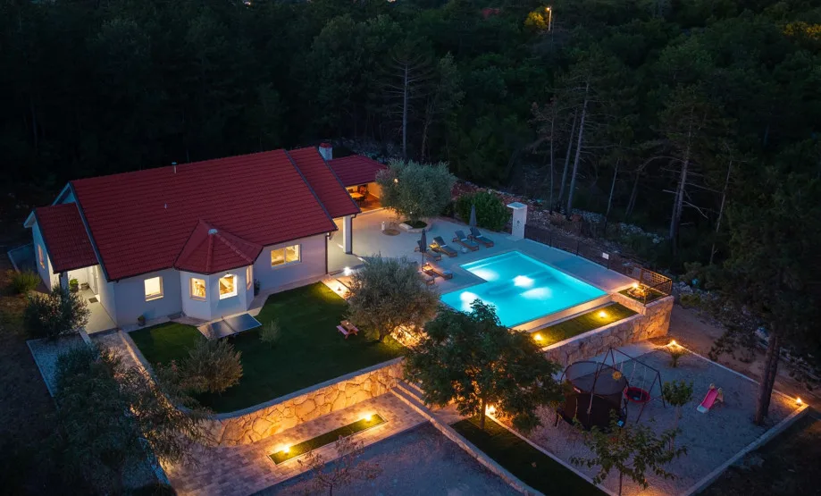 Vista aérea de la villa, la piscina y la parcela con césped, con un columpio y un tobogán.