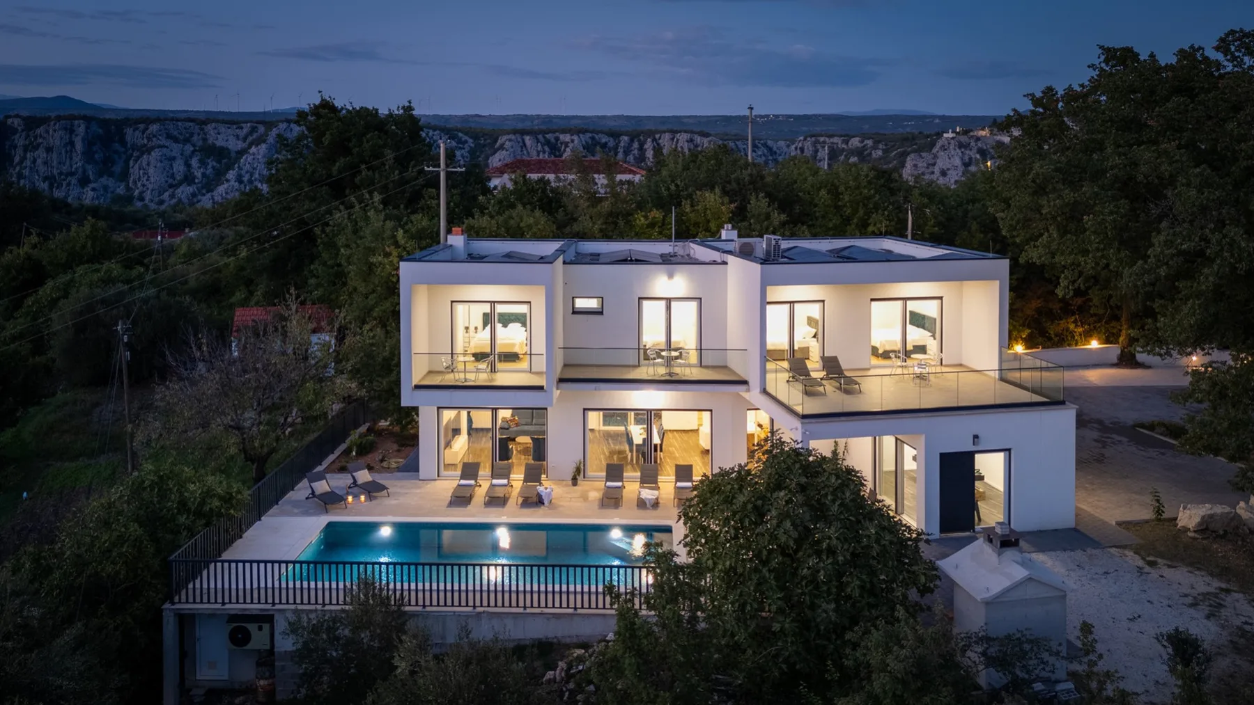 A modern house with a lit swimming pool on the terrace at dusk.