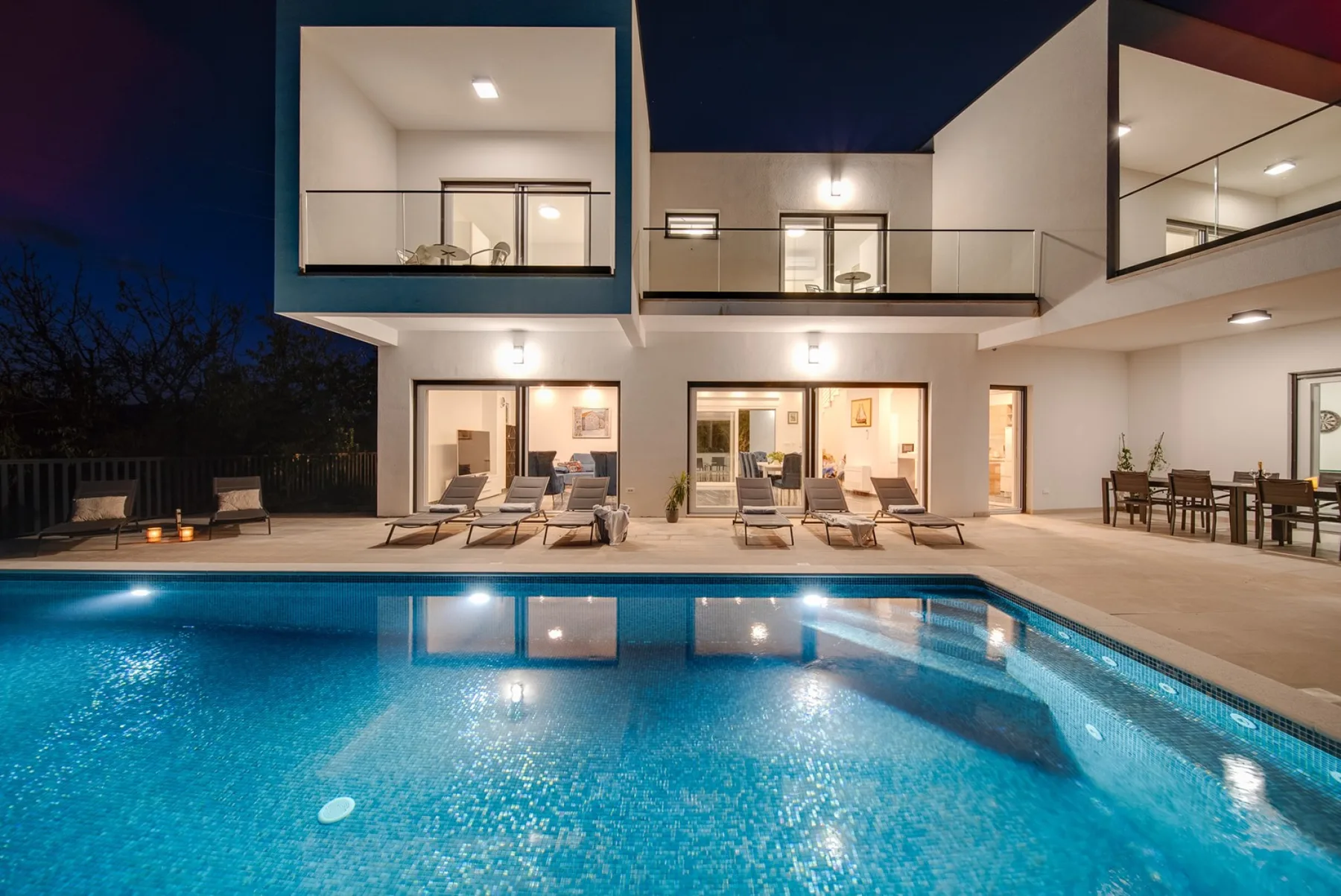 A modern house with a lit swimming pool and outdoor seating at dusk.