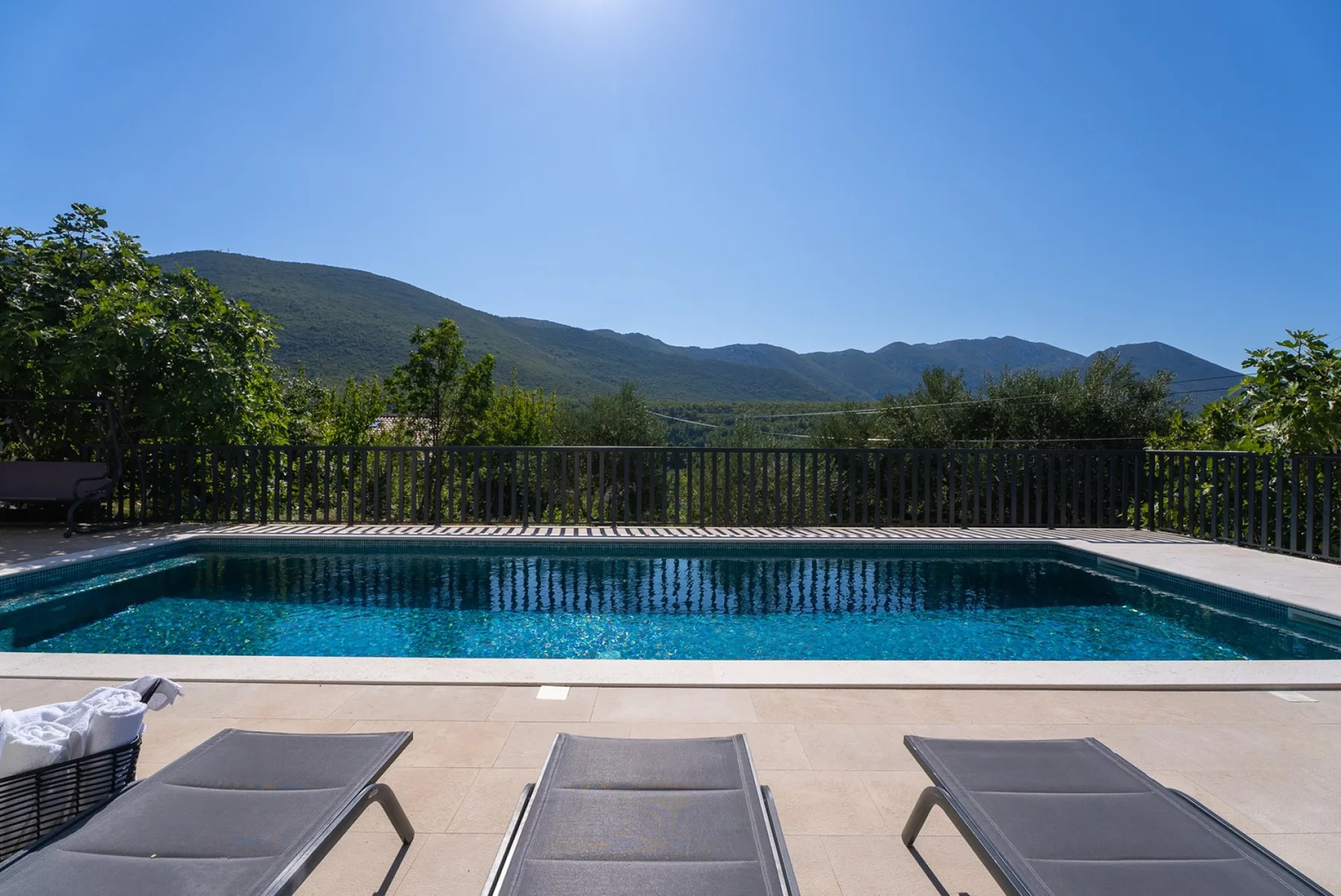 An outdoor swimming pool overlooks wooded hills, with loungers on the patio.