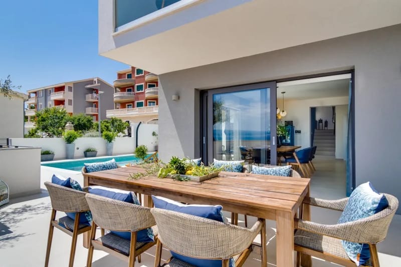 Una zona de comedor al aire libre con una mesa para 8 personas, una barbacoa, un televisor y un frigorífico