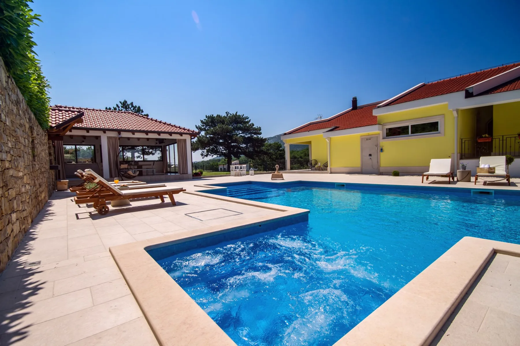 An outdoor swimming pool with a bubbling spa beside a yellow building.