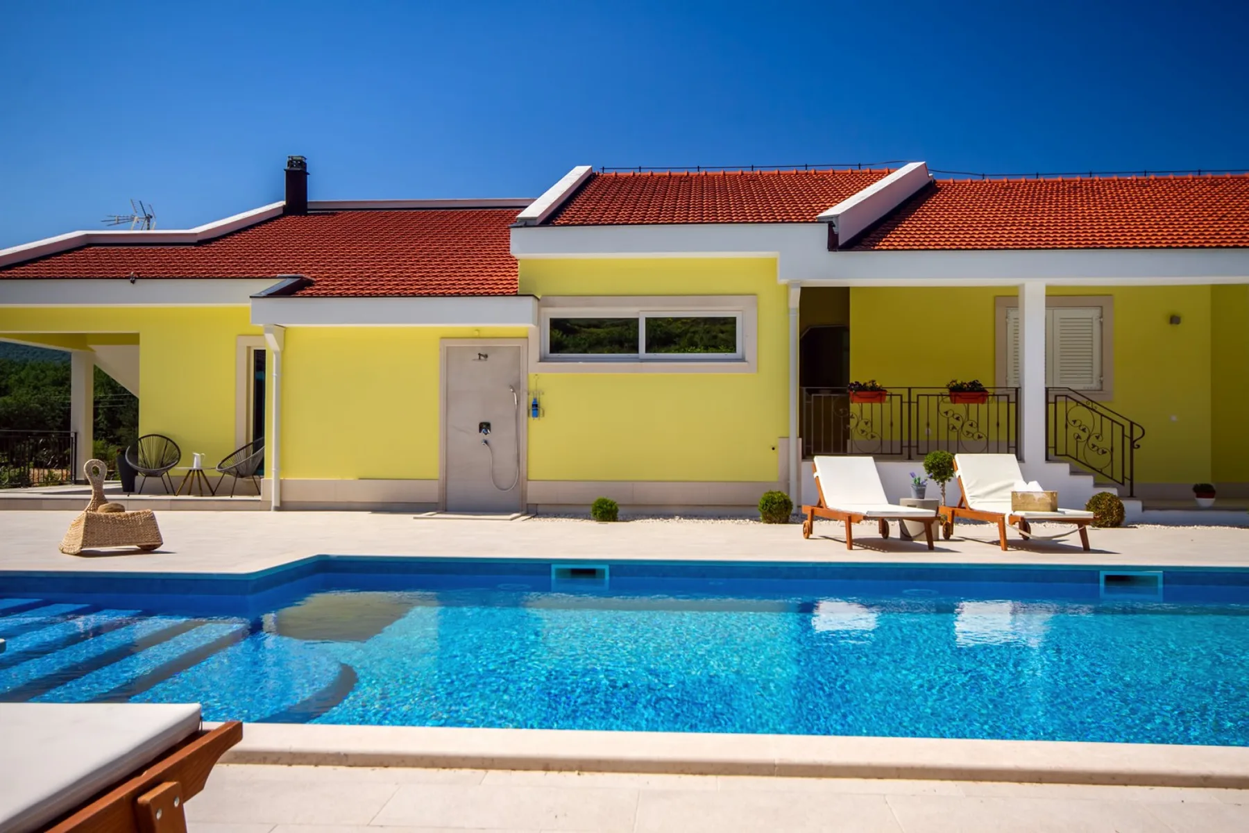 Una piscina frente a una casa amarilla con un patio cubierto.