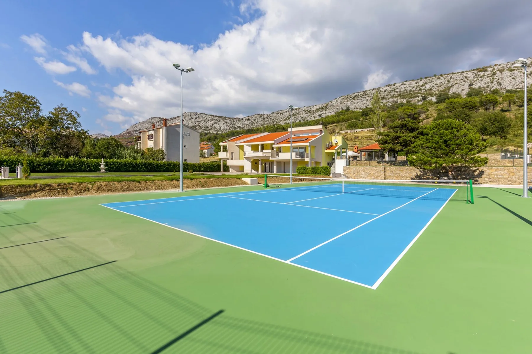Outdoor tennis court with a blue playing surface and green surround.