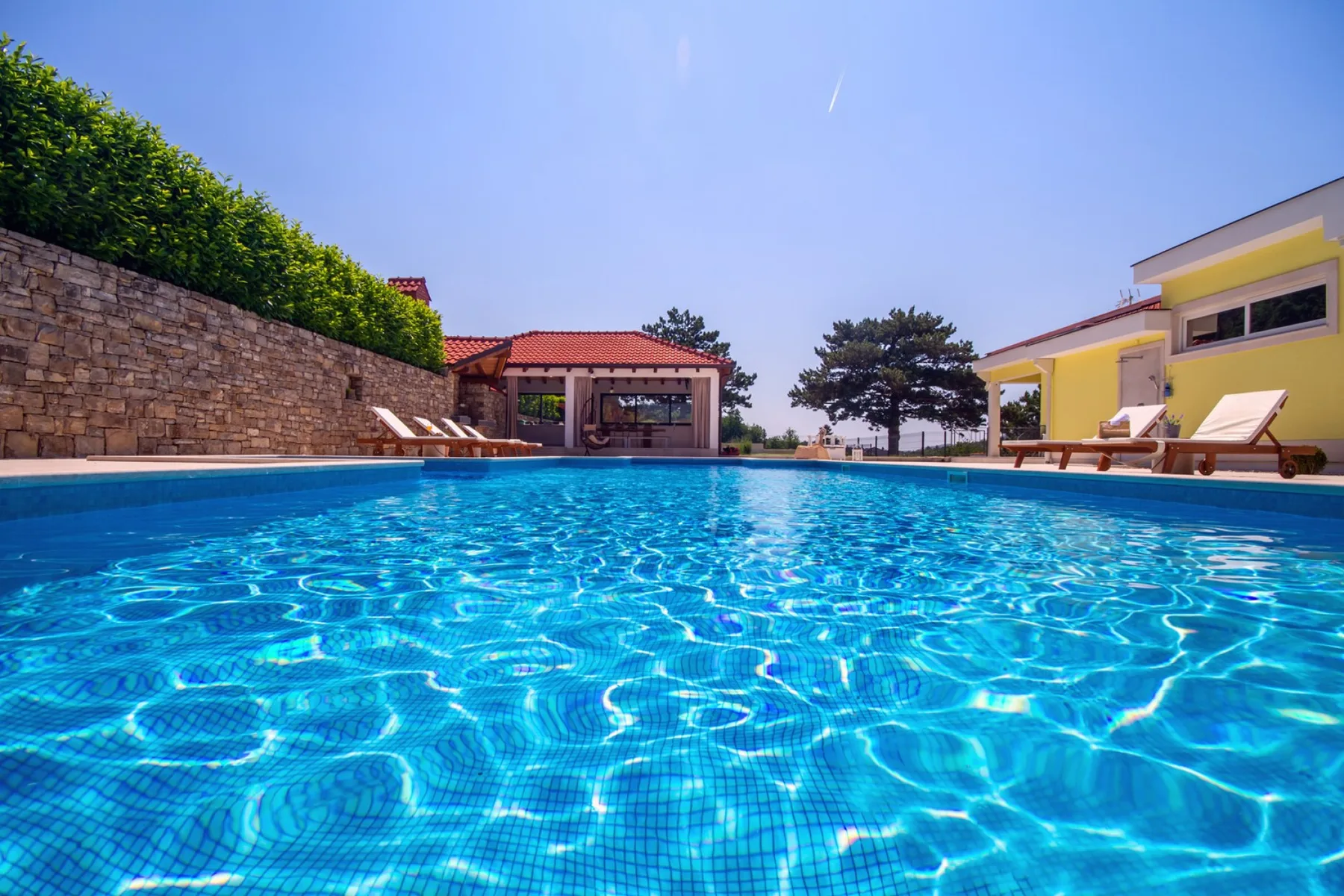 Una piscina al aire libre junto a un edificio amarillo, con asientos junto al borde.