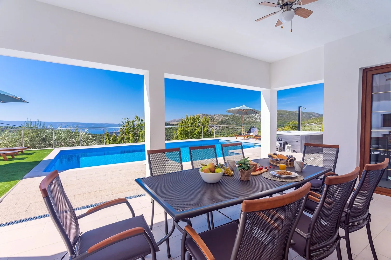 Covered outdoor dining area with a table and chairs overlooking a swimming pool.